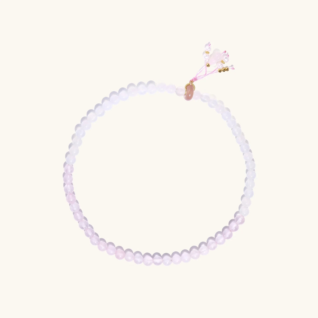 Double-wrap lavender beaded bracelet with rose quartz, pearls, gold vermeil charm and pink tassel on white background.