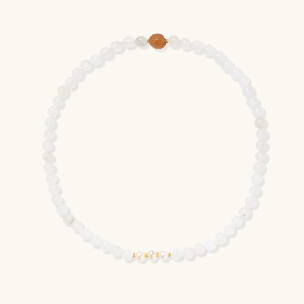 Three layered white beaded bracelets with carved orange agate lotus centerpiece and freshwater pearls on cream background.