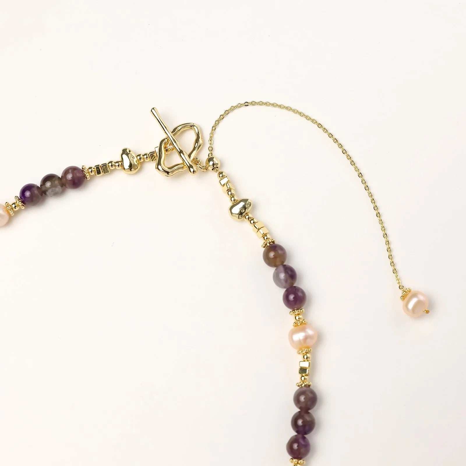 Gold necklace with iridescent baroque pearl pendant, purple amethyst beads, and crystal star charm on cream background