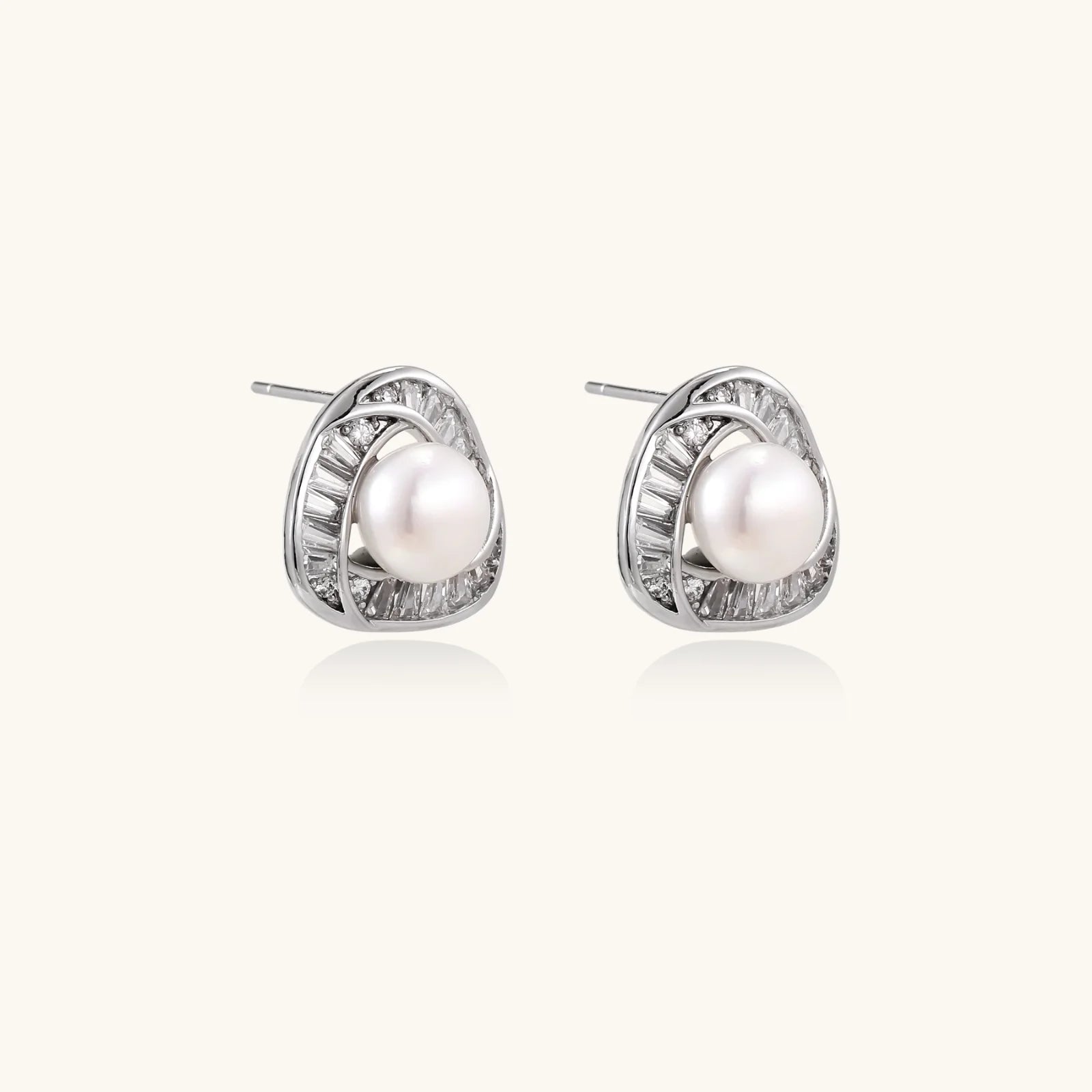 Triangular white gold plated stud earrings with central freshwater pearl and baguette-cut stones on white background