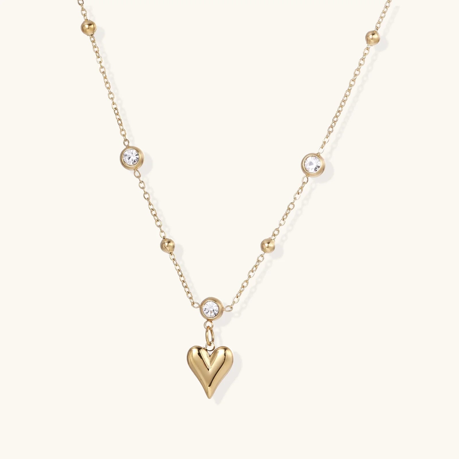 Delicate gold-plated necklace with bezel-set crystals and small heart pendant on beige background