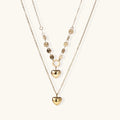 Three-layer 14K gold plated necklace with coin discs and dual heart pendants on cream background