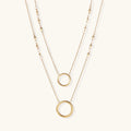 Layered gold necklace set with two open circle pendants and mixed chain styles on beige background