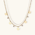 Gold layered necklace set with engraved heart pendants and crystal accents on cream background