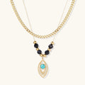 Layered gold necklace with turquoise evil eye pendant and black quartz beads on cream background