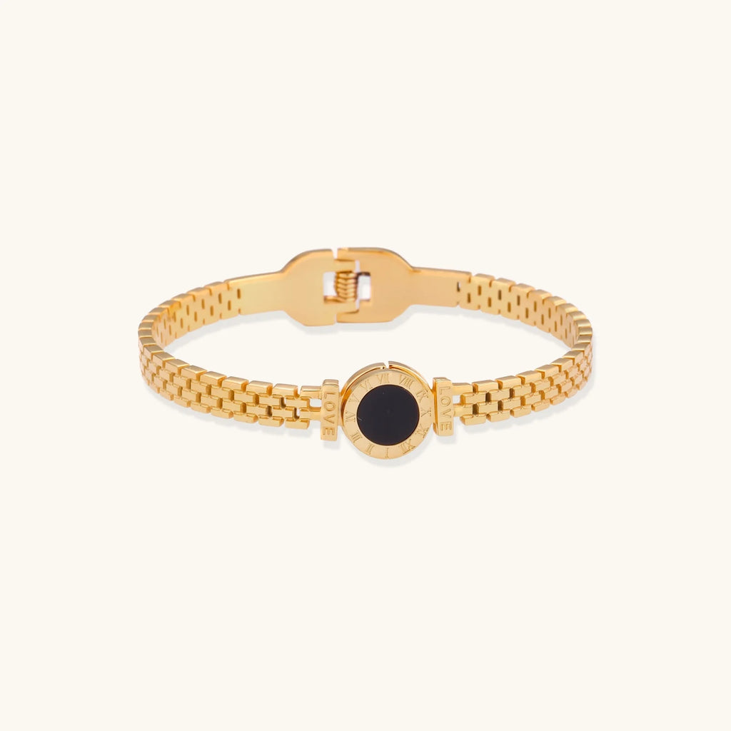 Gold mesh bracelet with circular black mother of pearl medallion featuring Roman numeral engravings and hinged clasp