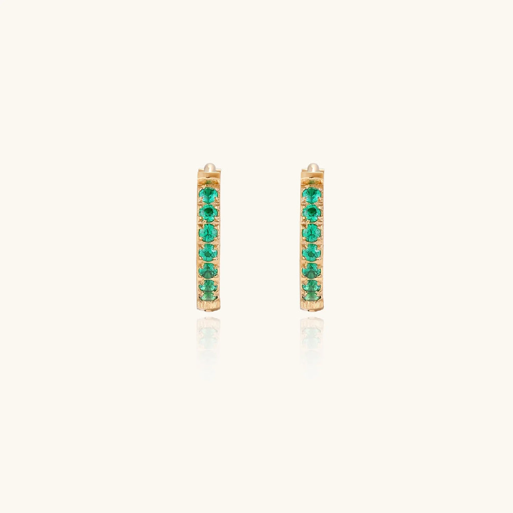 Pair of small gold huggie hoop earrings with bright green cubic zirconia stones on cream background