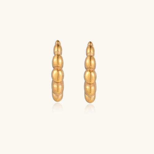 Gold-plated sculptural hoop earrings with chunky segmented design on cream background