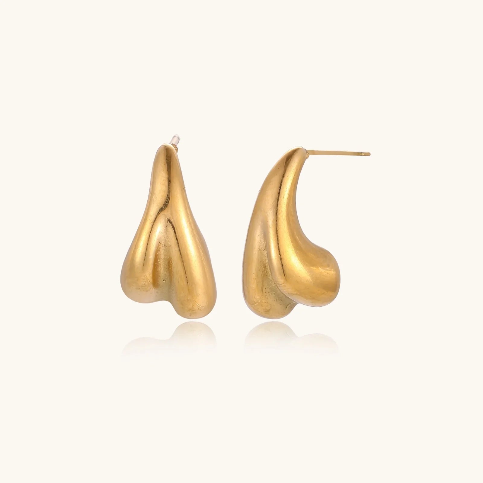 Pair of sculptural gold stud earrings with twisted organic forms on cream background