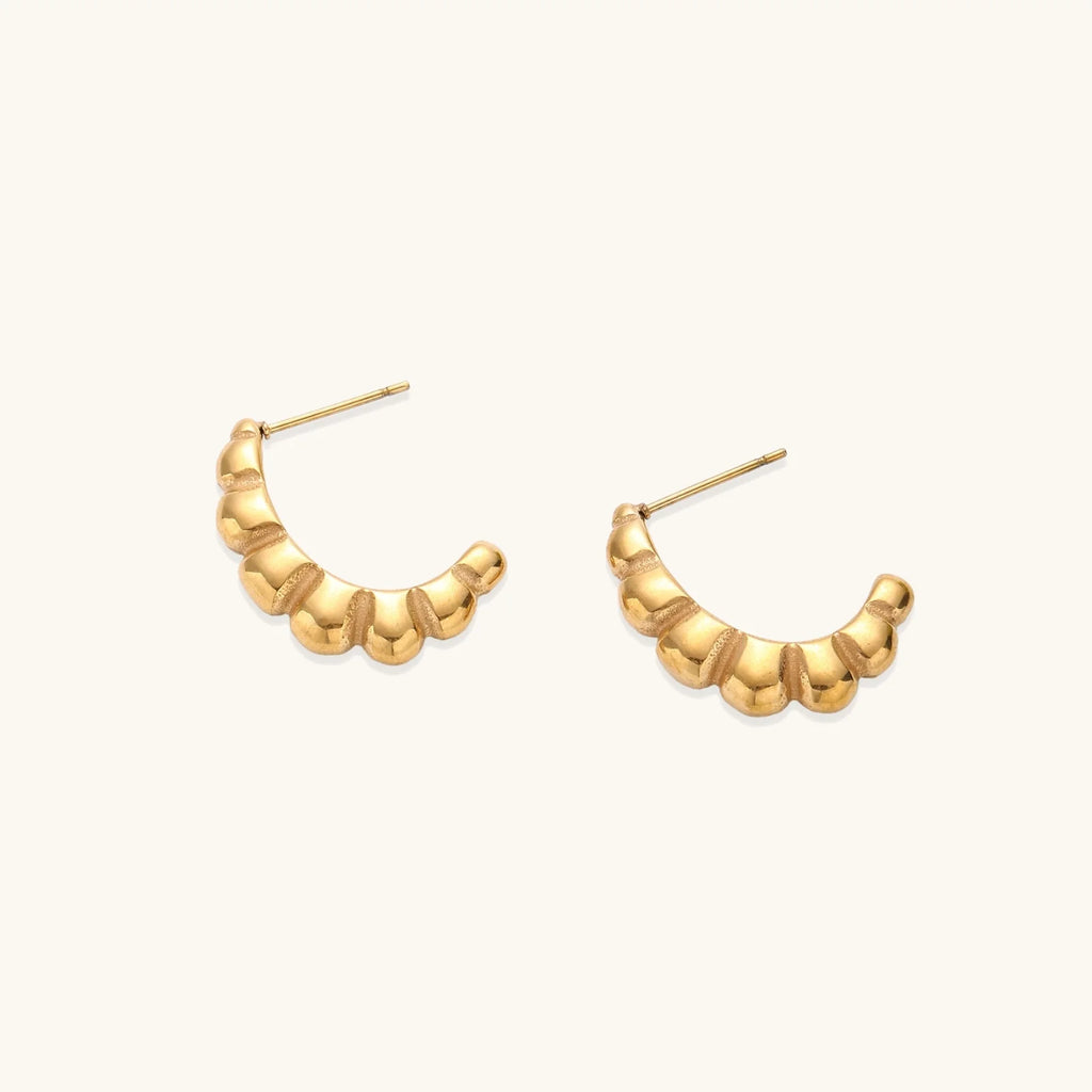 Gold-plated sculptural hoop earrings with chunky segmented design on cream background